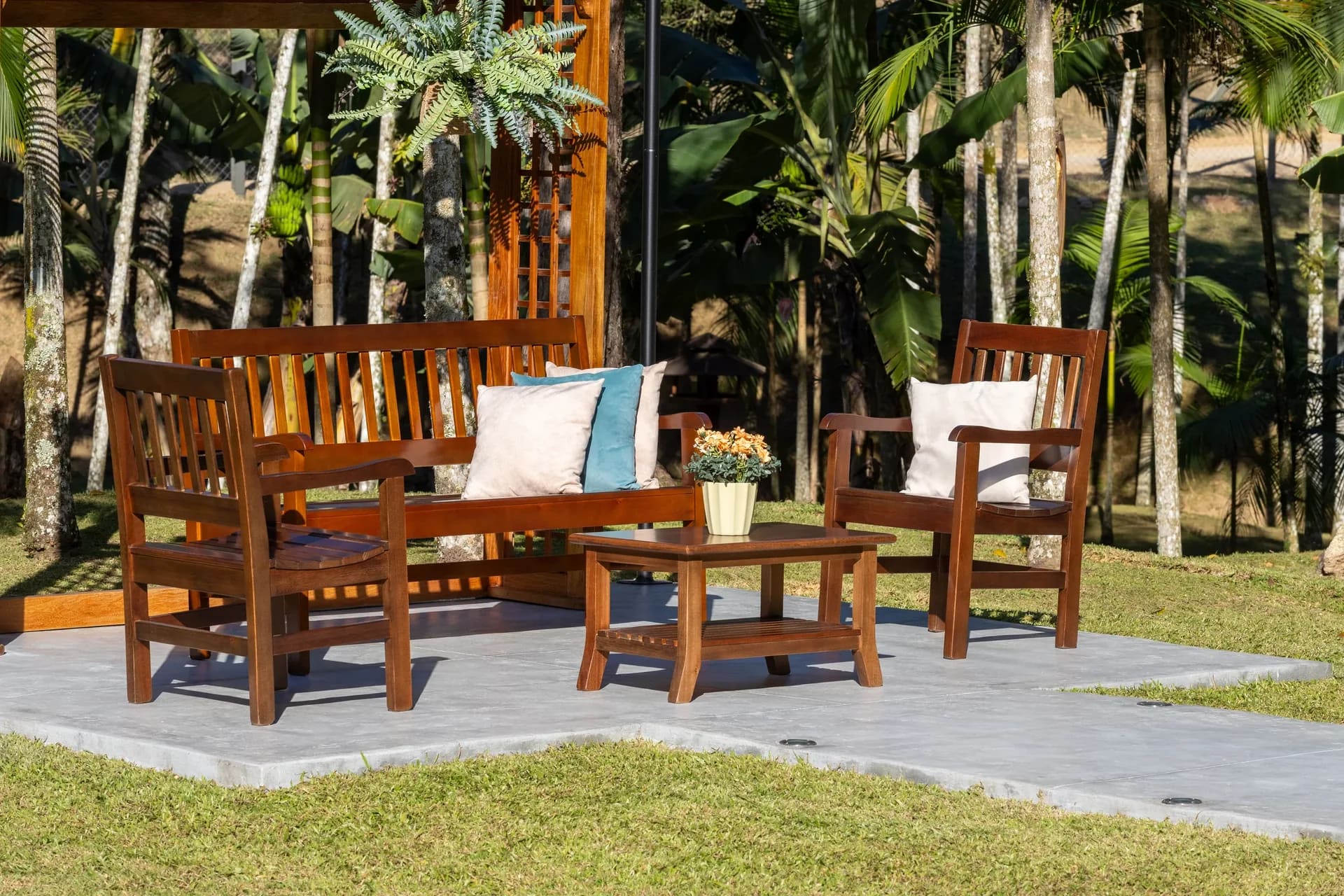 Sofá, poltronas e mesa de centro de madeira da Móveis Daniella em um jardim com palmeiras